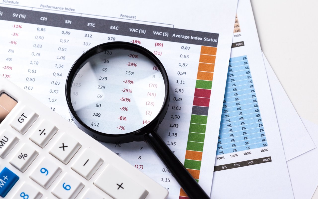 Magnifying glass over financial tables beside a calculator.