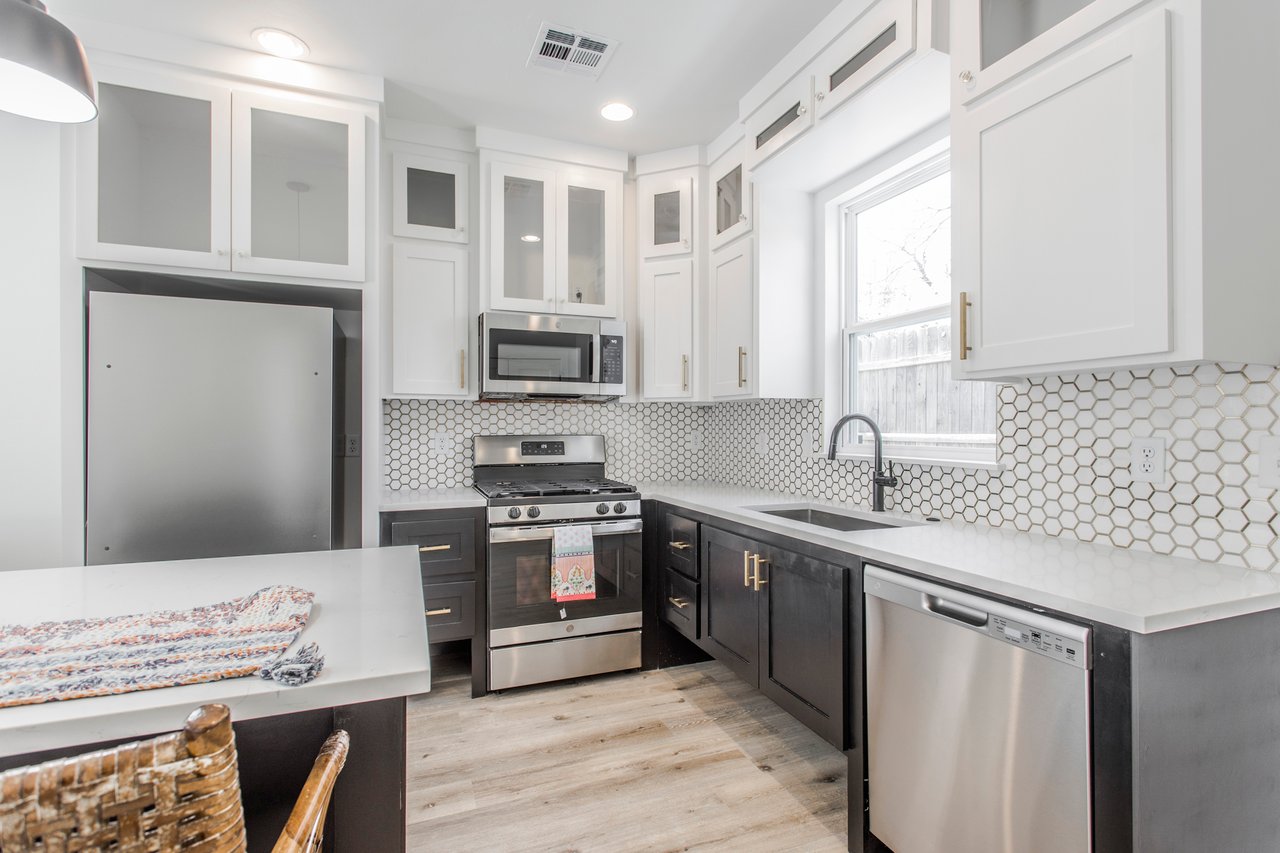 Renovated kitchen with dark lower cabinets, white hexagonal backsplash, and stainless-steel appliances.