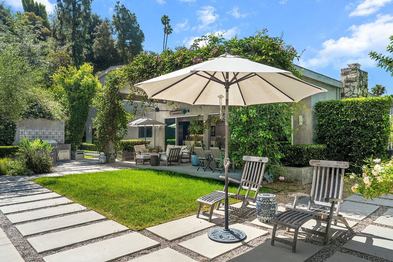 Backyard patio with a large white umbrella, lawn, outdoor seating, and built-in kitchen.