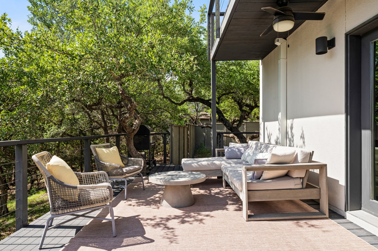 Covered deck with cushioned lounge seating and woven chairs overlooking mature trees.