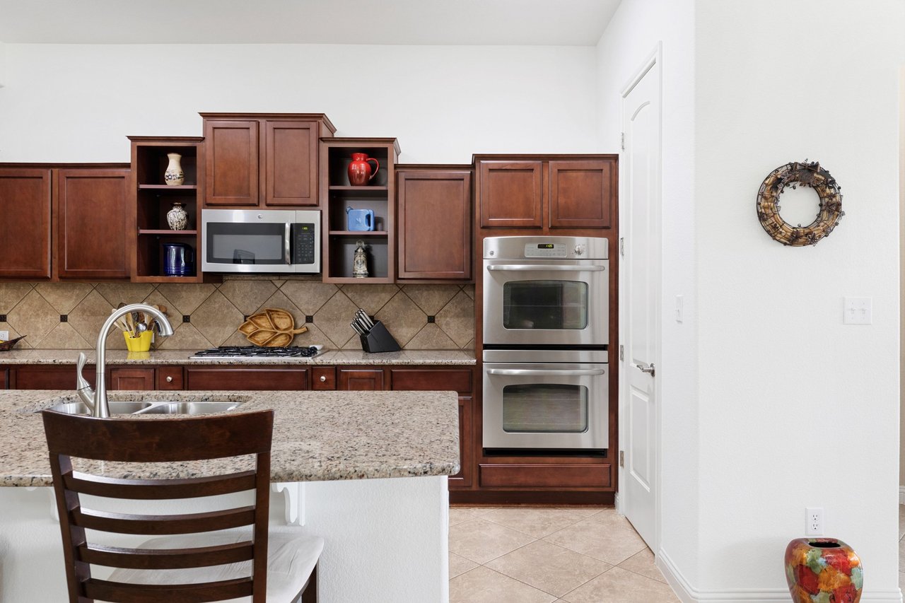 Kitchen with dark cherry cabinets, granite island, tiled backsplash, and stainless steel double wall oven.