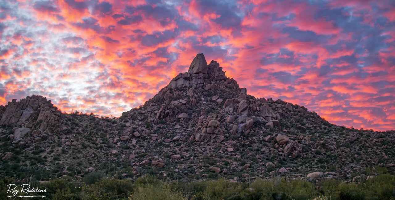Rocky desert mountain beneath vivid pink and orange sunset clouds.
