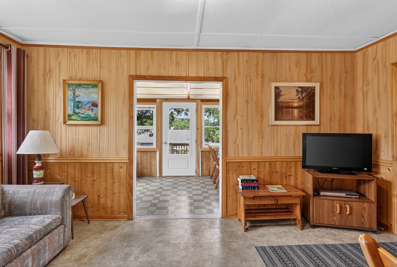 Wood-paneled living room with a patterned sofa, television, and doorway to a bright adjoining room.