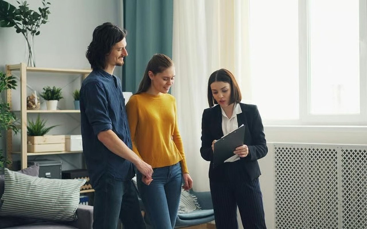 Real estate agent reviewing a clipboard with a couple in a bright living room.
