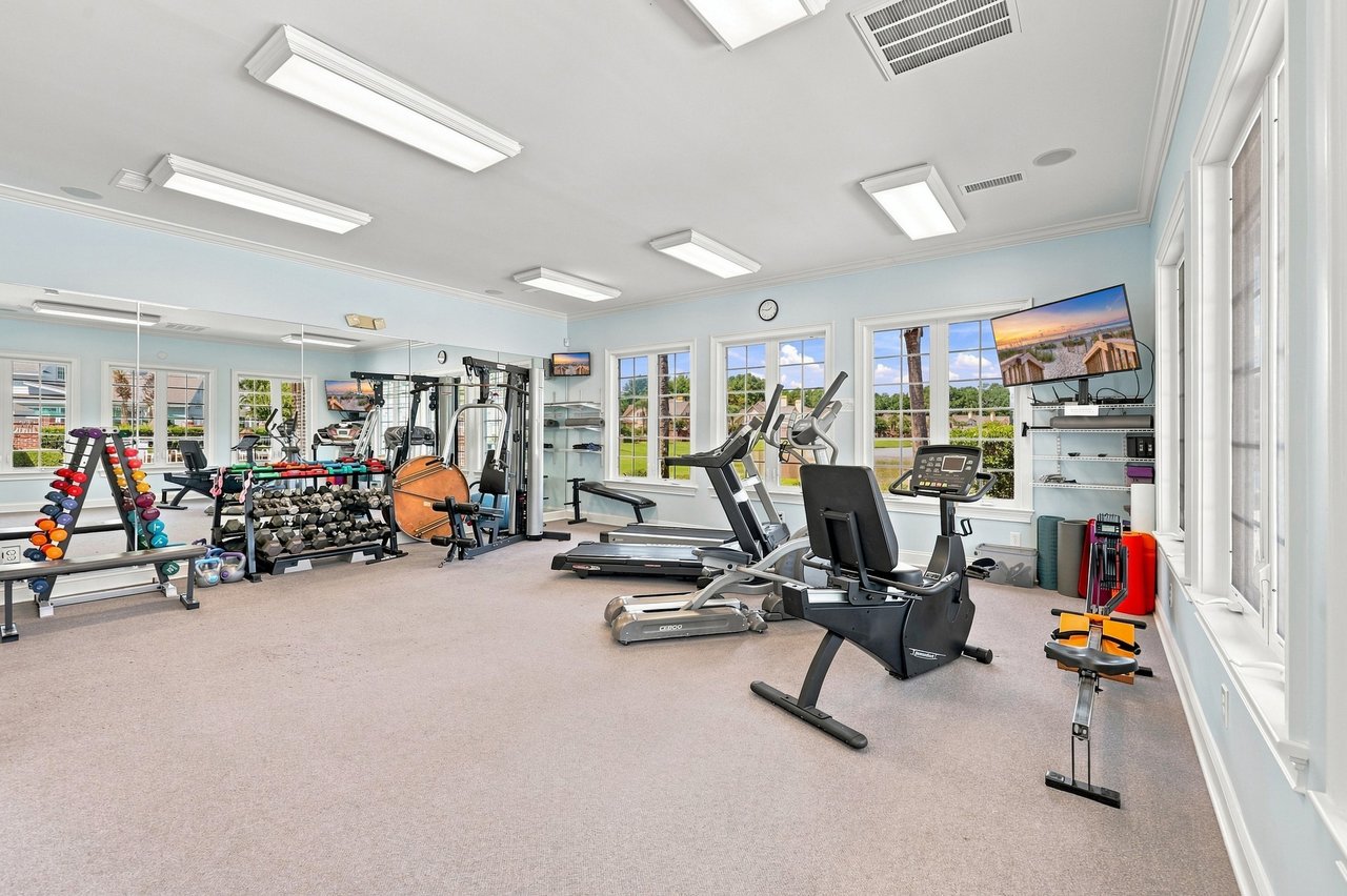 Community fitness room with treadmills, weight machines, and large windows overlooking green grounds.
