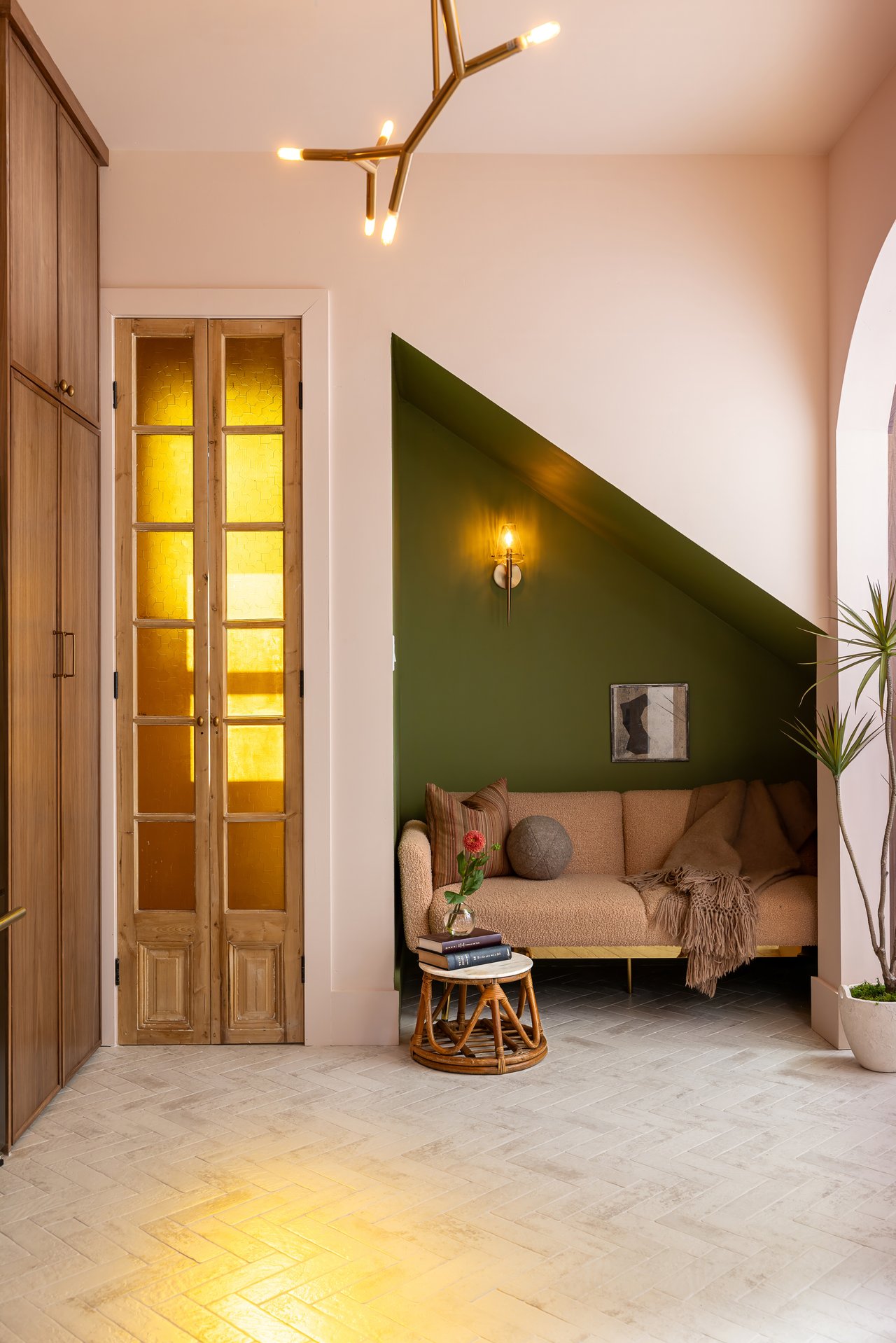 Sitting nook with a beige sofa against a deep green wall beside golden-glass wooden doors.