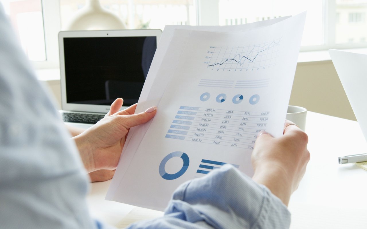 Person reviews a printed report with blue charts beside an open laptop.