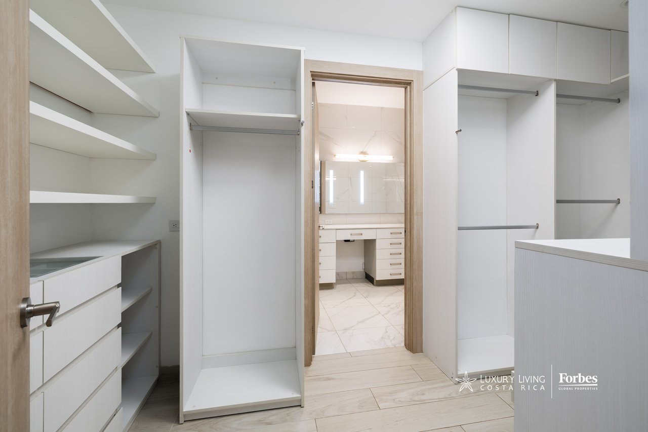 Walk-in closet with built-in shelving and hanging space, opening to a marble-floored bathroom.