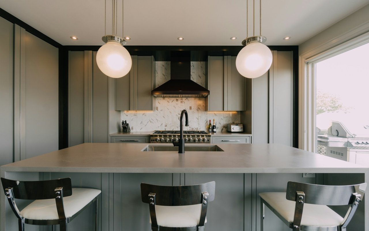 Modern kitchen with a large stone island, gray cabinetry, marble-pattern backsplash, and two globe pendants.