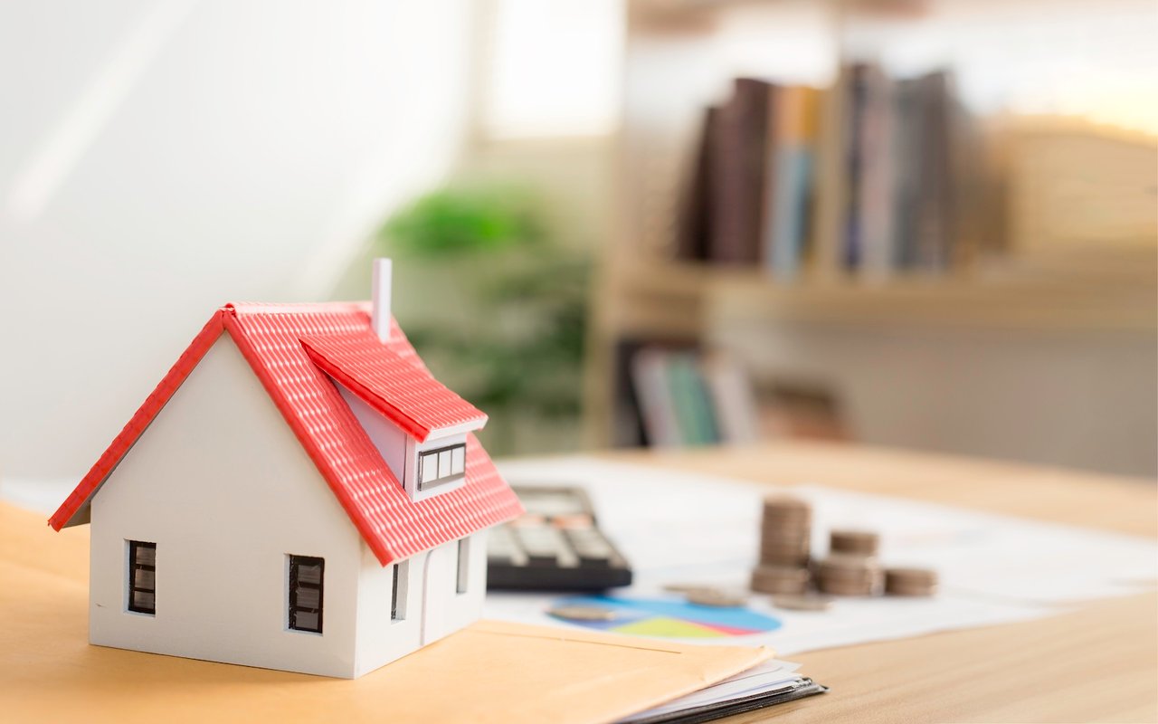 Miniature house model on desk with paperwork and calculator, representing the home buying process.