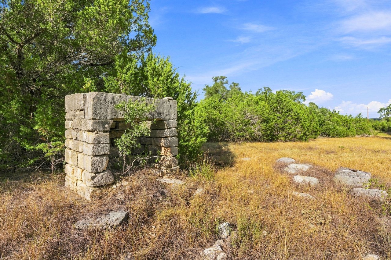 Hill Country land with a weathered stone structure, scattered rocks, and golden grass.