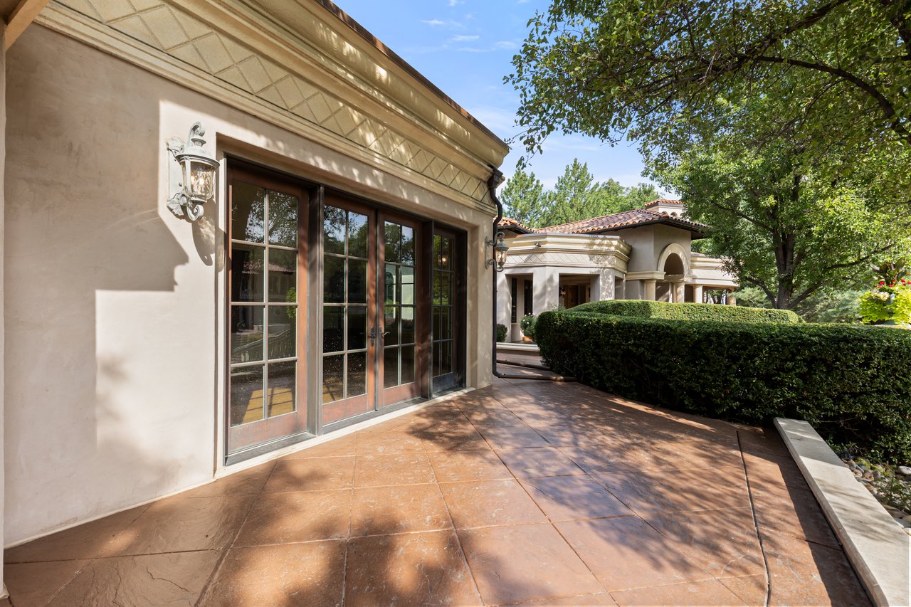 Estate patio with tall glass-paneled doors, terracotta tile, and a clipped hedge.