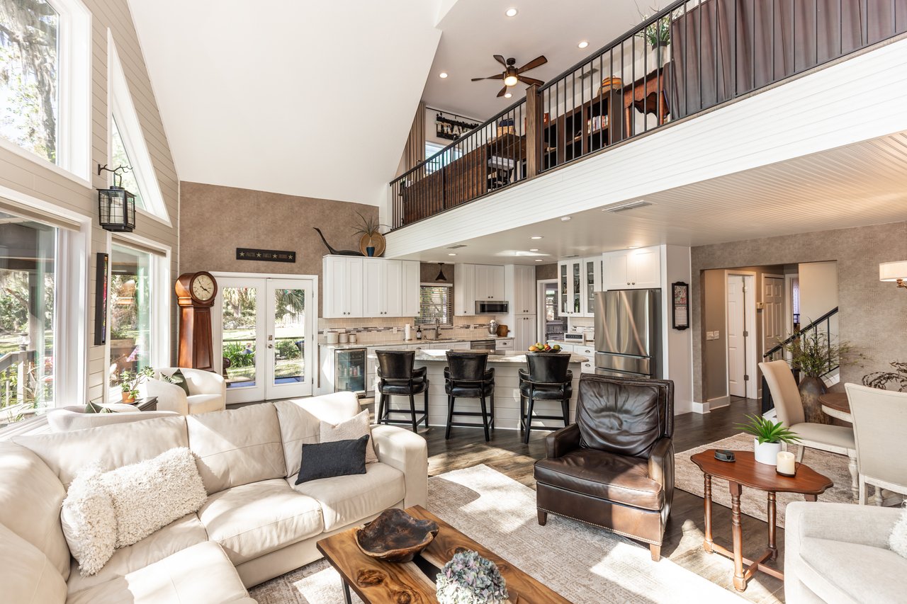 Open-plan living room and kitchen with a loft mezzanine, double-height ceiling, and large windows.