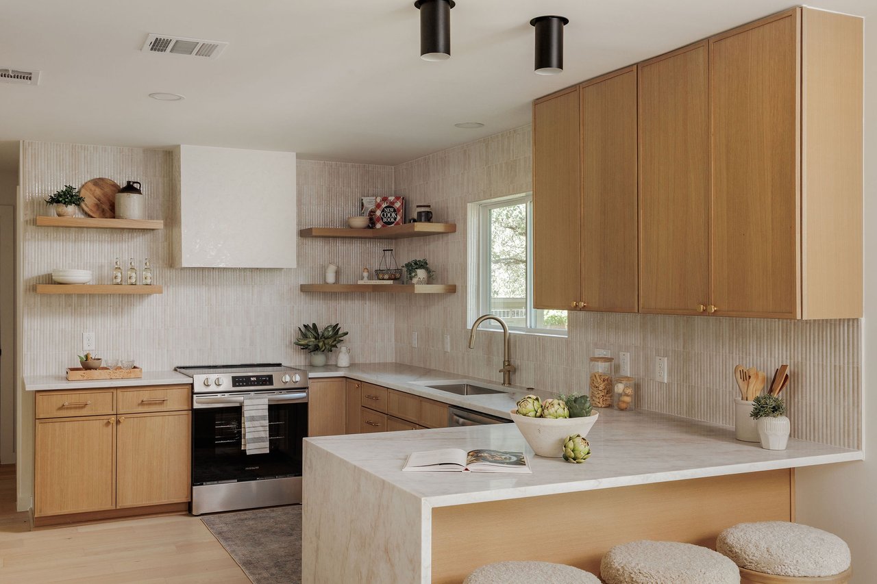 Staged kitchen with light oak cabinets, marble island, open shelves, and a window over the sink.