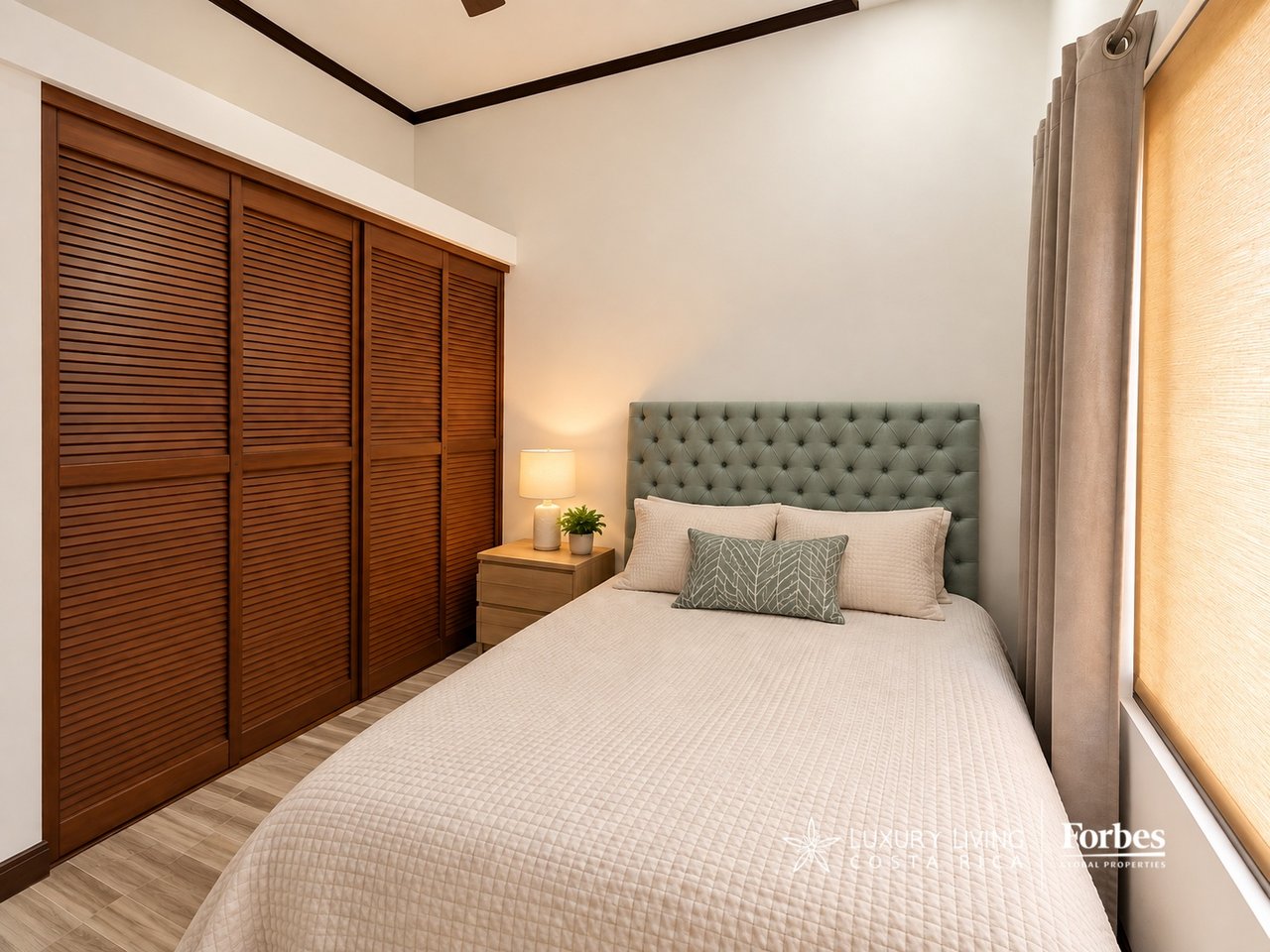 Bedroom with a tufted gray headboard beside wooden louvered closet doors.