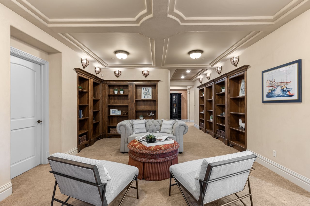 Home library with dark built-in bookshelves, a coffered ceiling, and a central seating area.