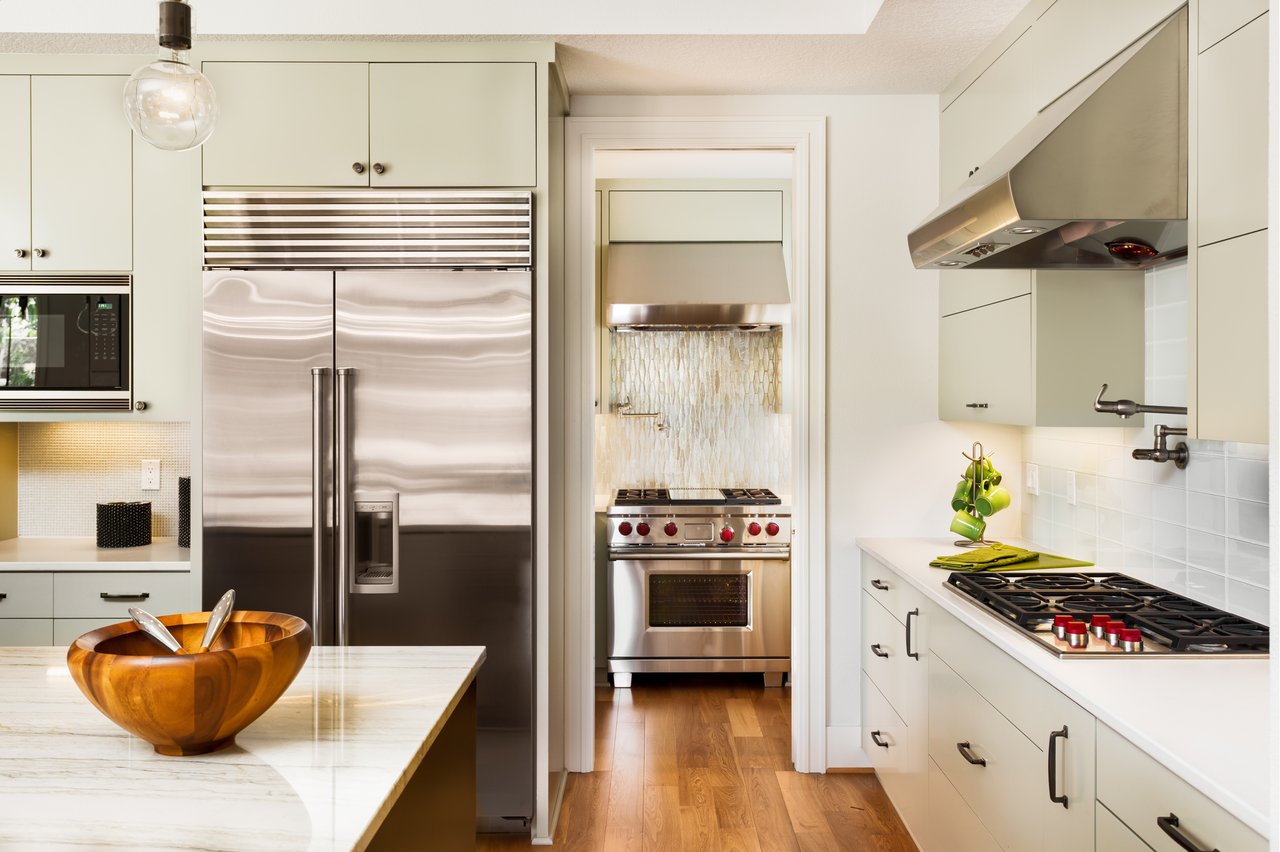 Modern kitchen with pale cabinets, stainless steel appliances, marble island, and wood floors.