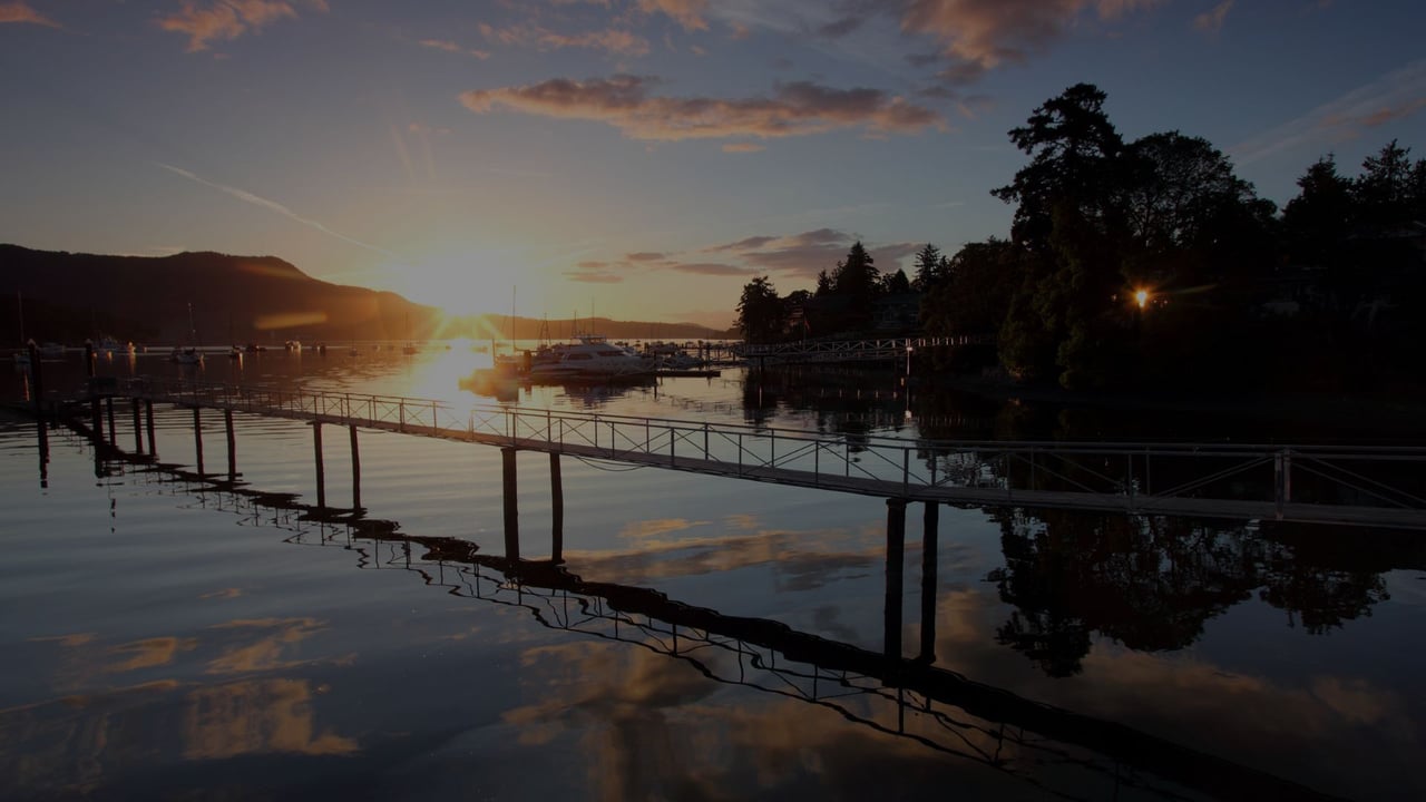 Marina at dusk with boats, a long pier, and sunset reflected on calm water.
