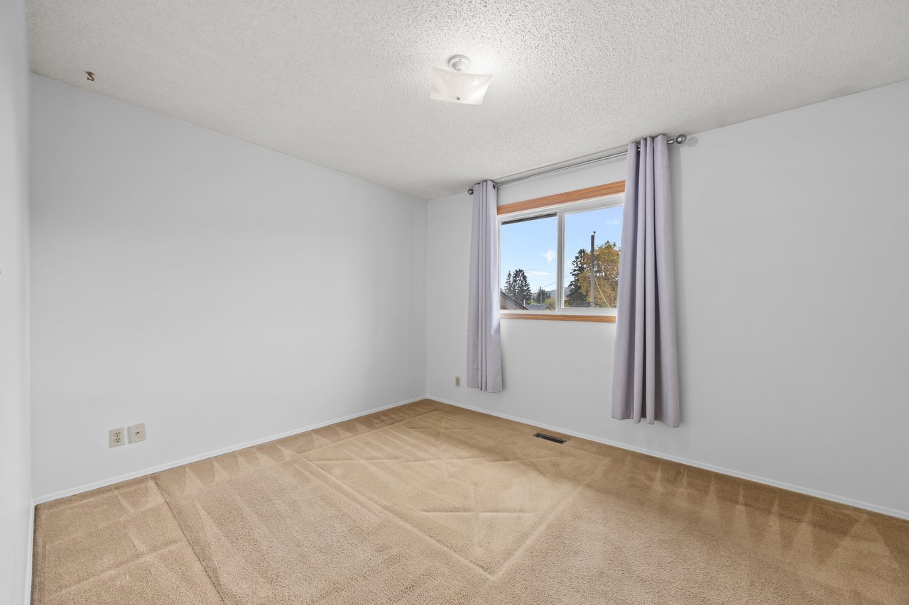Empty bedroom with beige carpet and a curtained window.