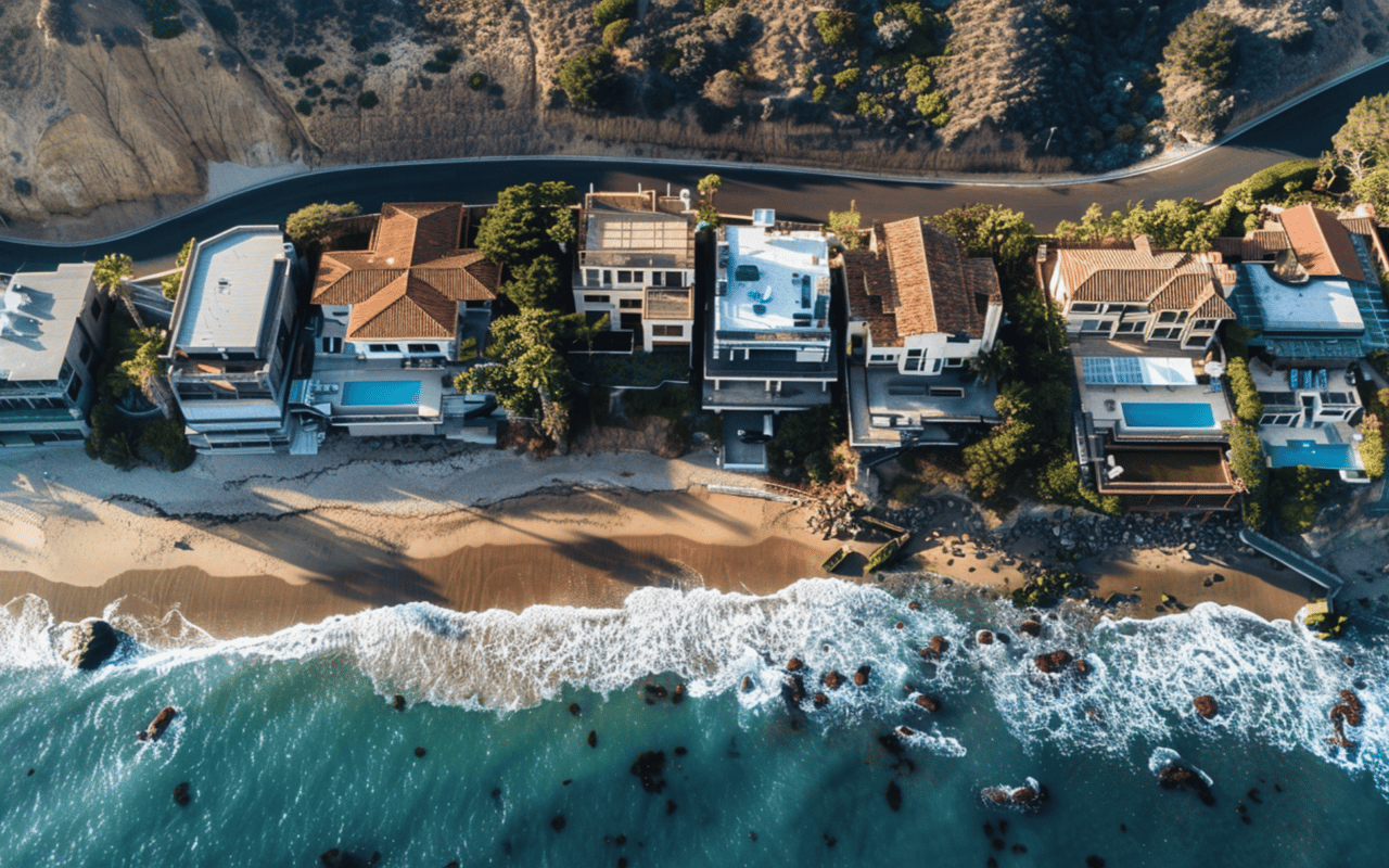 Aerial view of waterfront homes lining a sandy beach beside turquoise water.