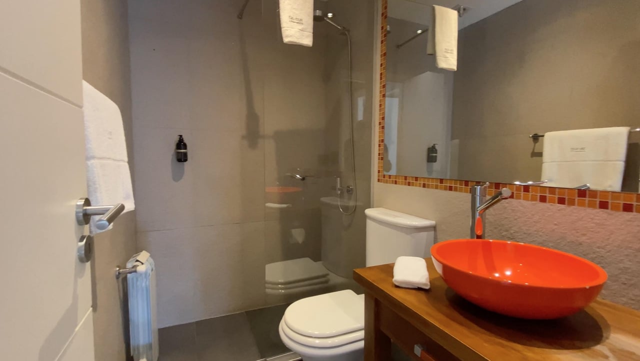 Bathroom with a bright orange vessel sink on a wooden vanity beside a glass-enclosed shower.
