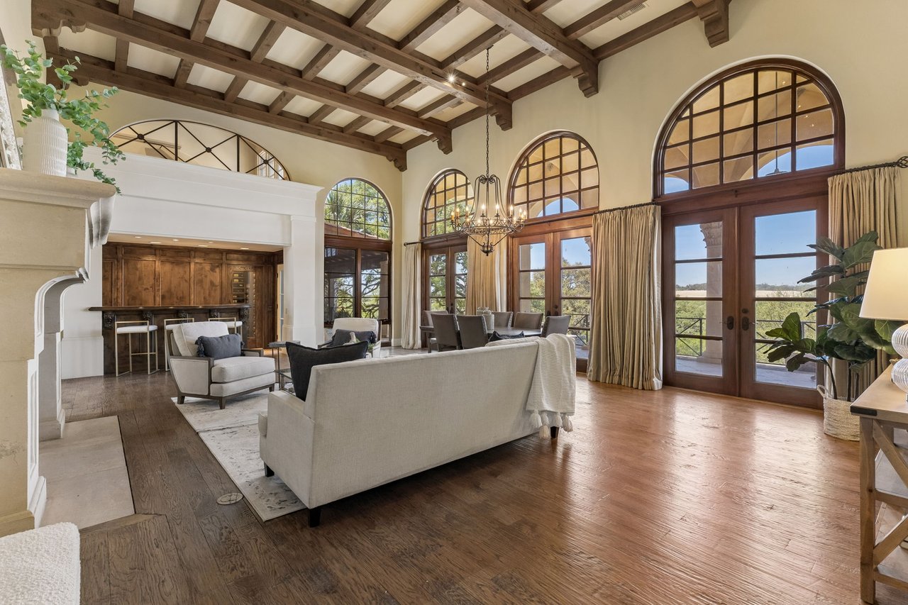 Living room with exposed wood beams, arched windows, a stone fireplace, and a furnished sitting area.