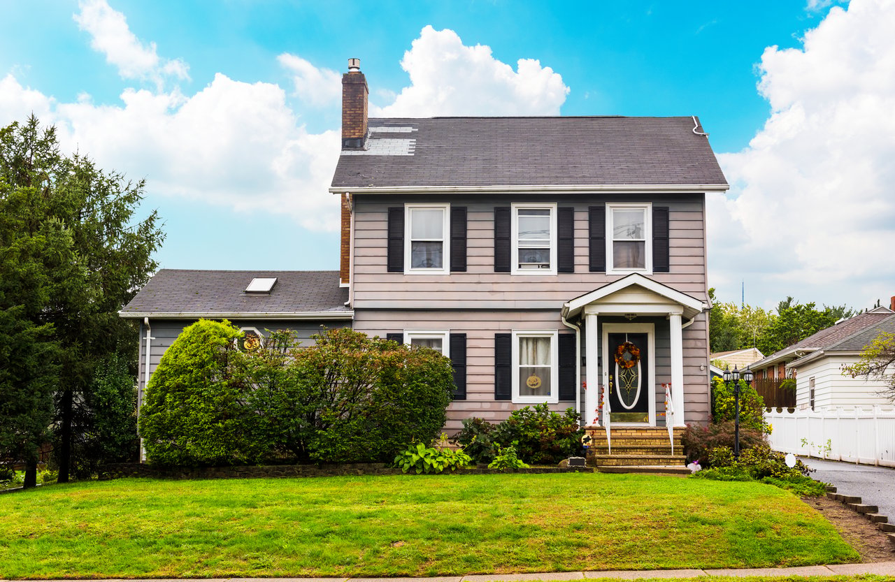 Two-story gray house with black shutters, a covered entry, and a broad green lawn.