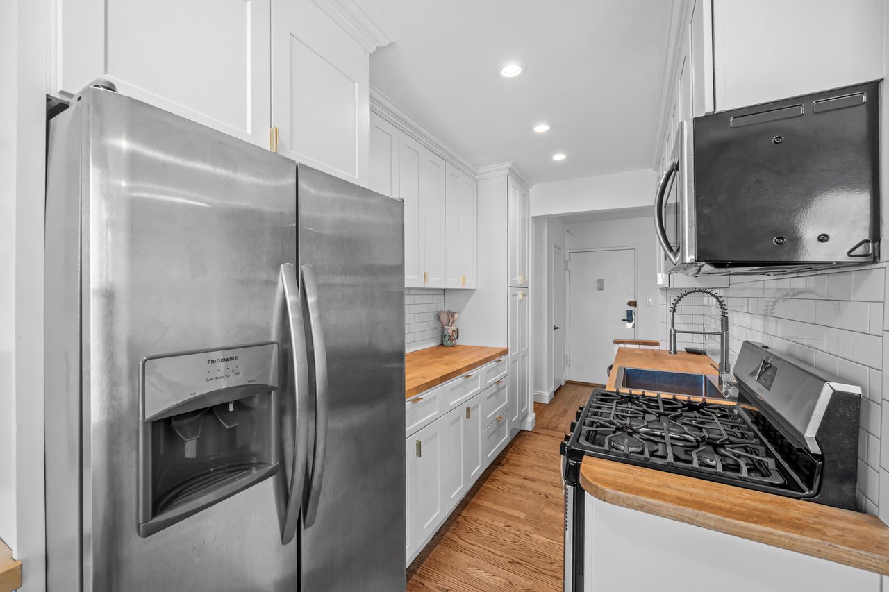 Kitchen with white cabinets, butcher-block counters, stainless appliances, and hardwood floors.