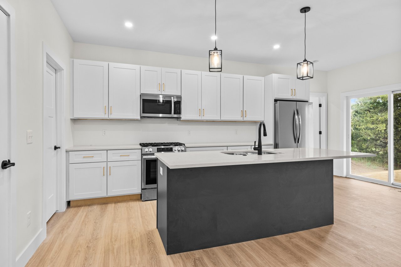 Kitchen with white shaker cabinets, stainless steel appliances, and a large dark island beside sliding glass doors.