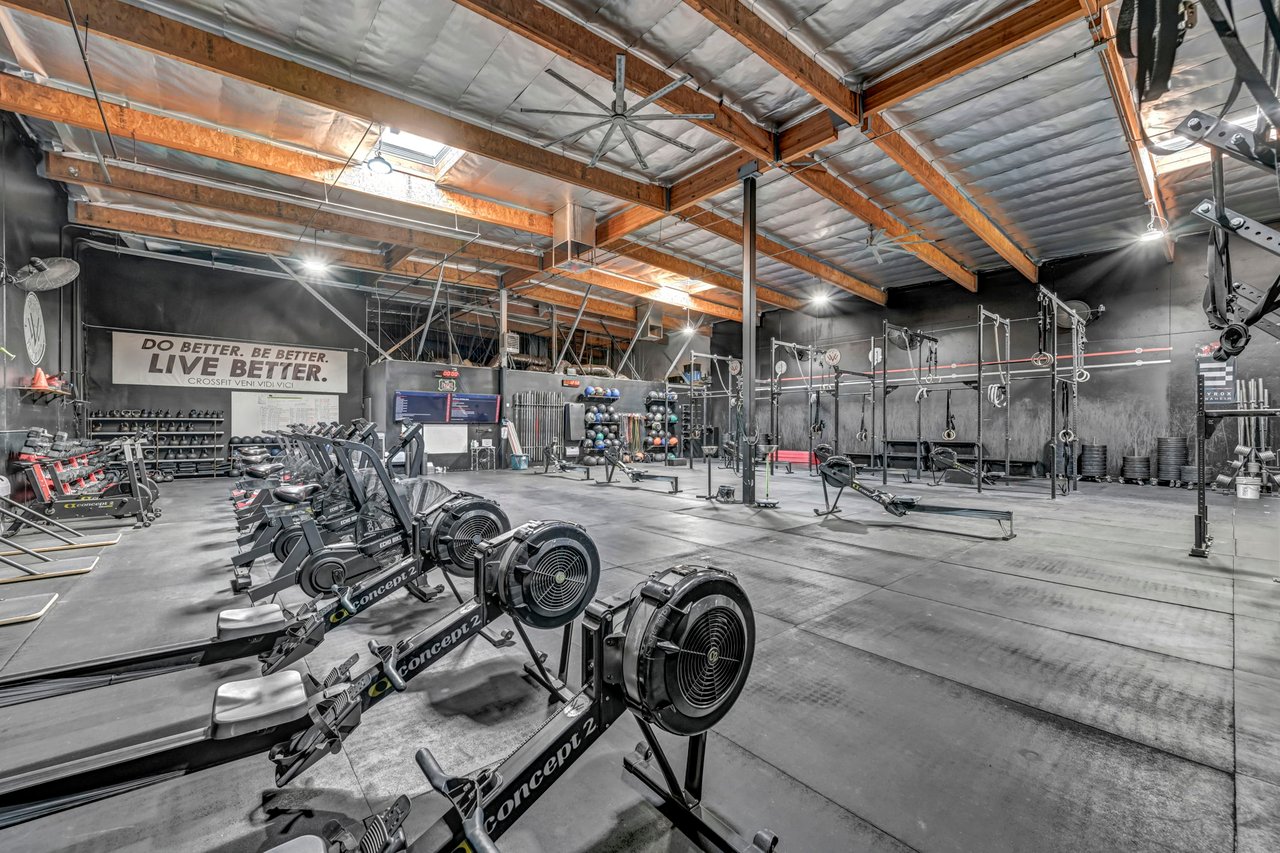 Gym interior with rowing machines, weightlifting racks, and exposed timber ceiling beams.