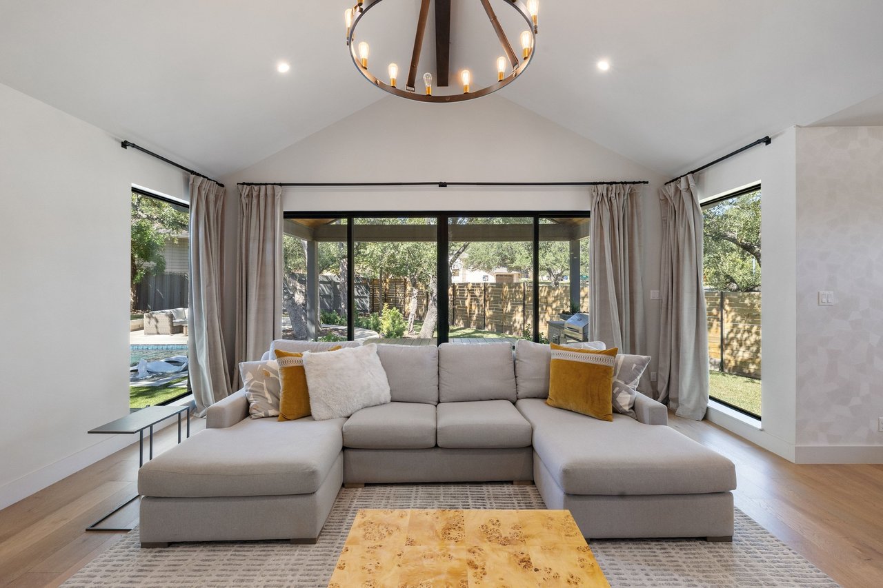 Living room with a gray sectional beneath a vaulted ceiling and windows overlooking the backyard pool.