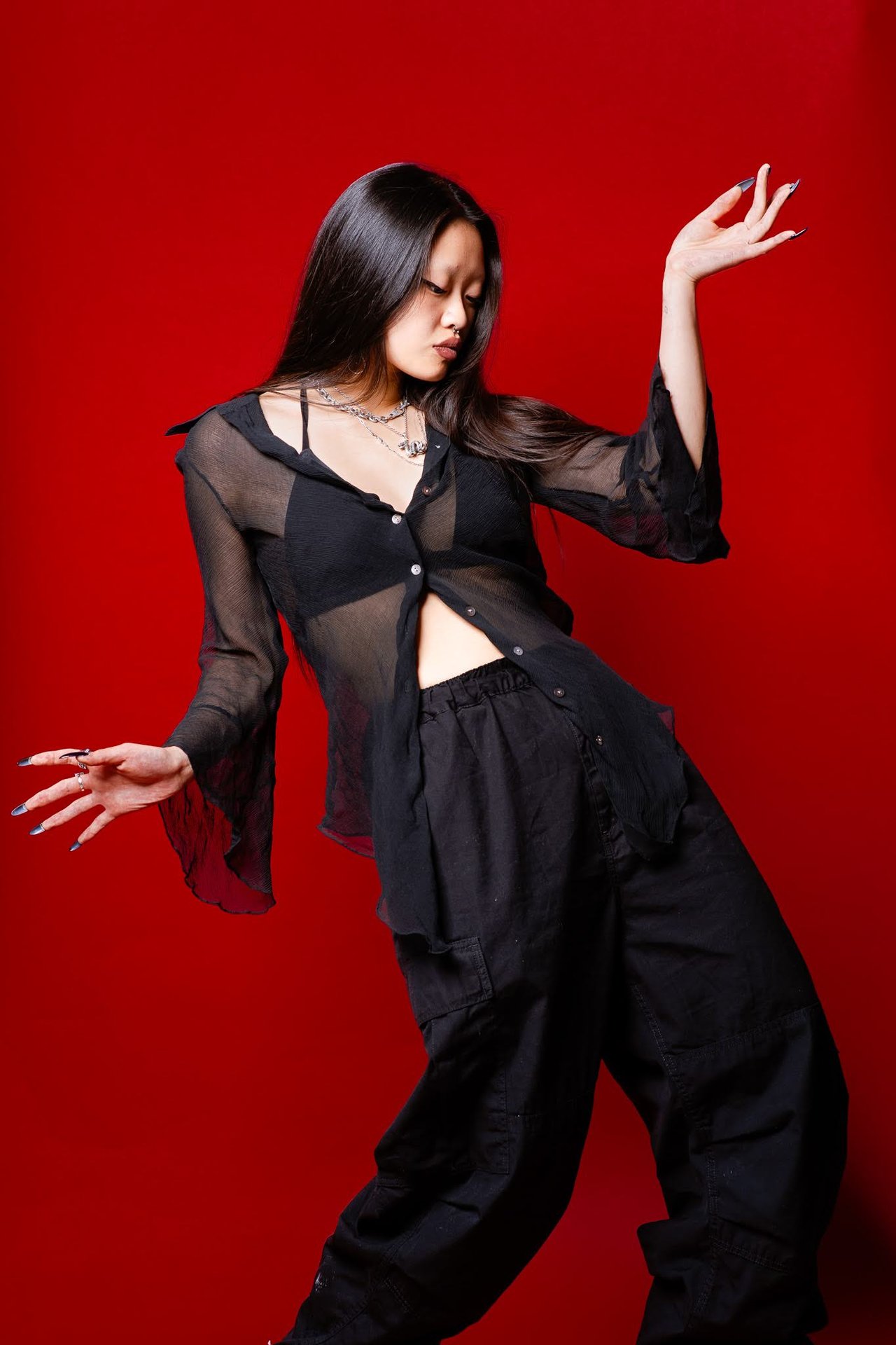 Dancer Jin poses with both arms extended against a vivid red backdrop.