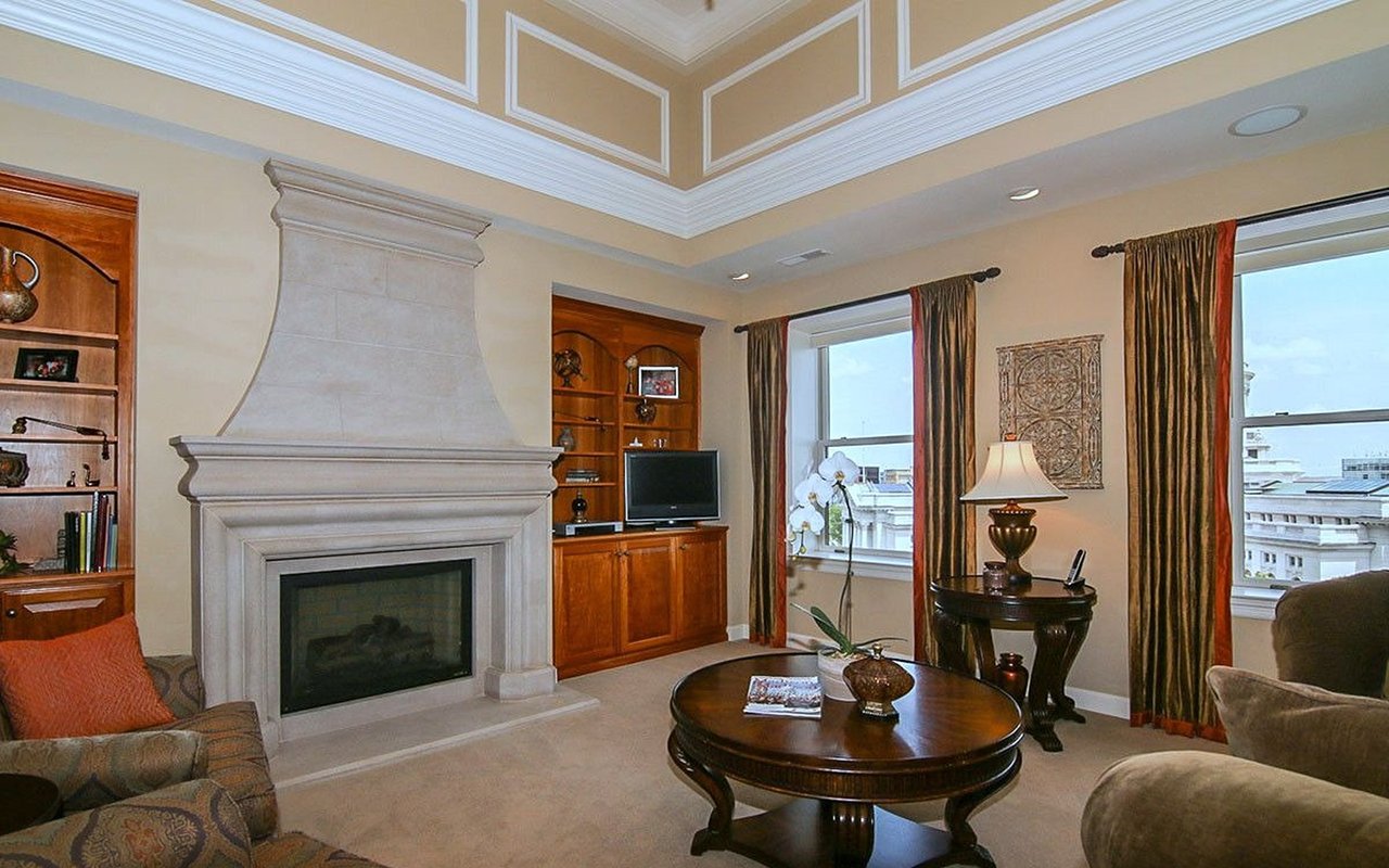 Penthouse living room with a stone fireplace, built-in wooden cabinetry, and tall windows overlooking nearby buildings.