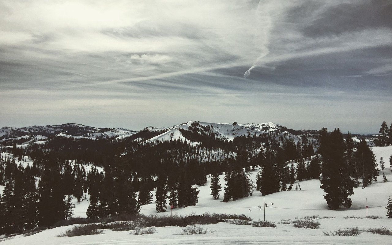 Snow-covered mountain ridges and evergreen forest beneath a cloudy sky.