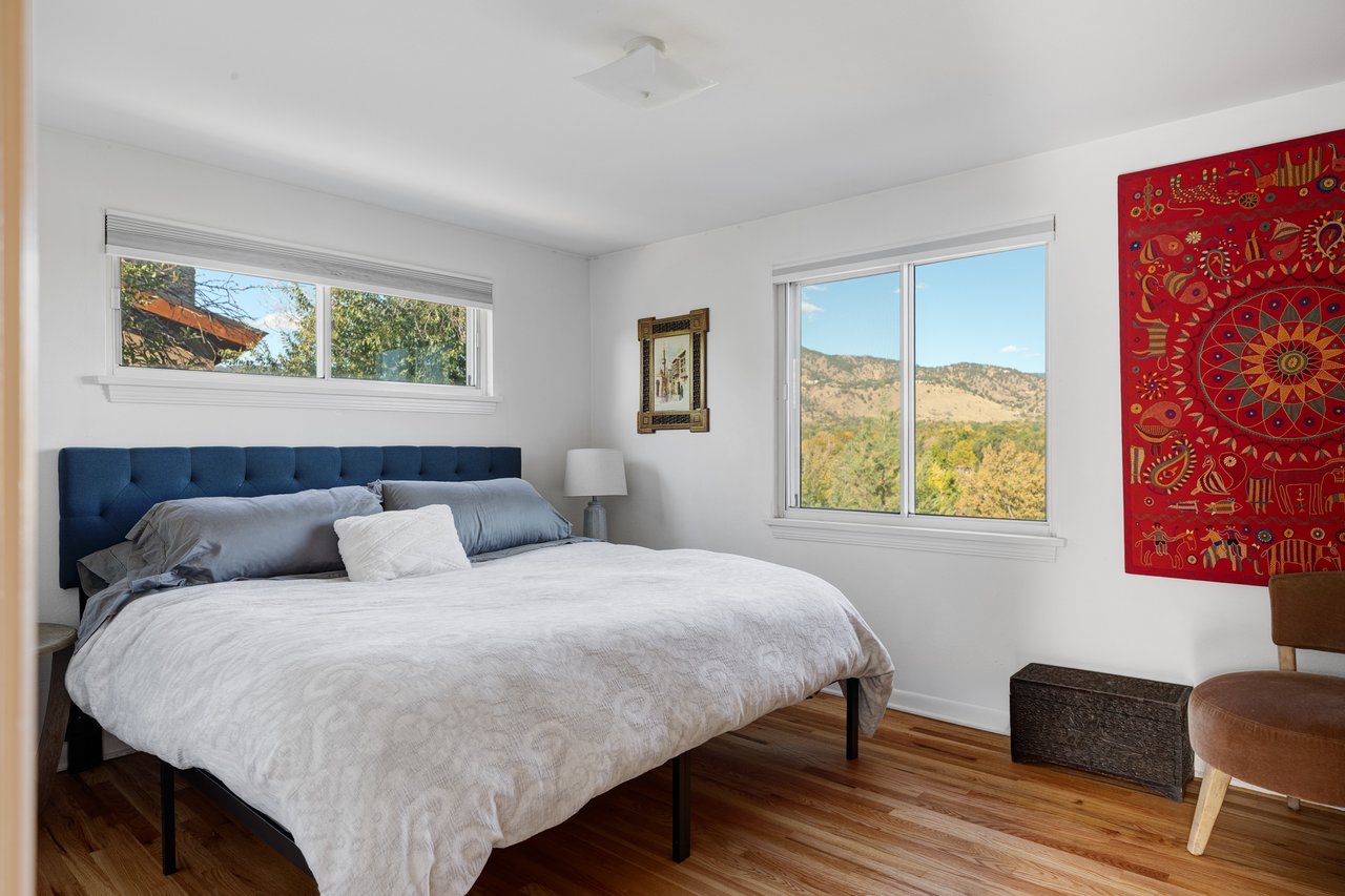 Bedroom at 2003 Balsam Drive with hardwood floors, a red textile wall hanging, and windows facing the foothills