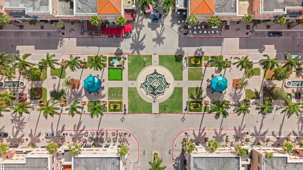 Mizner Park’s landscaped plaza and circular fountain, surrounded by palm trees and shops.