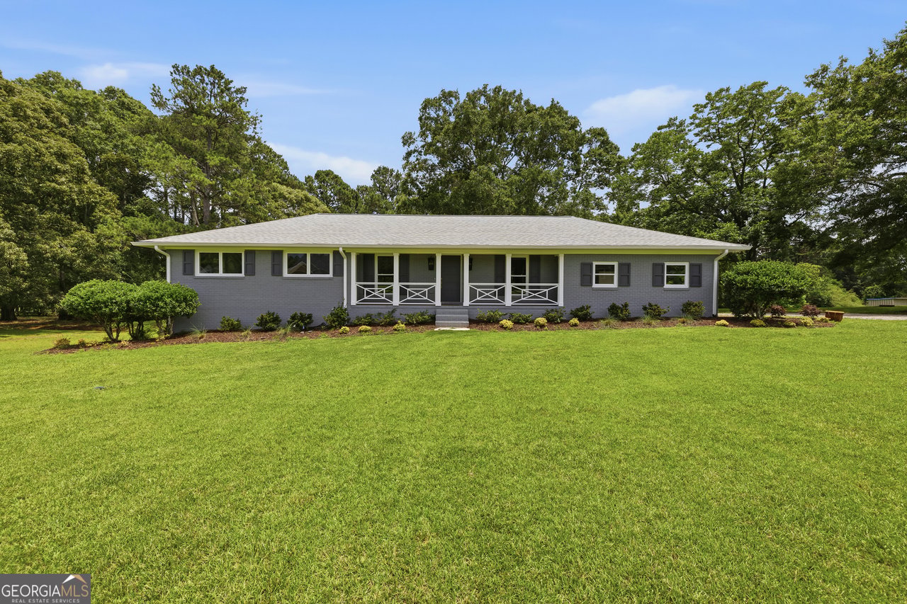 Gray single-story home with a long covered porch, white railings, and a broad green lawn.