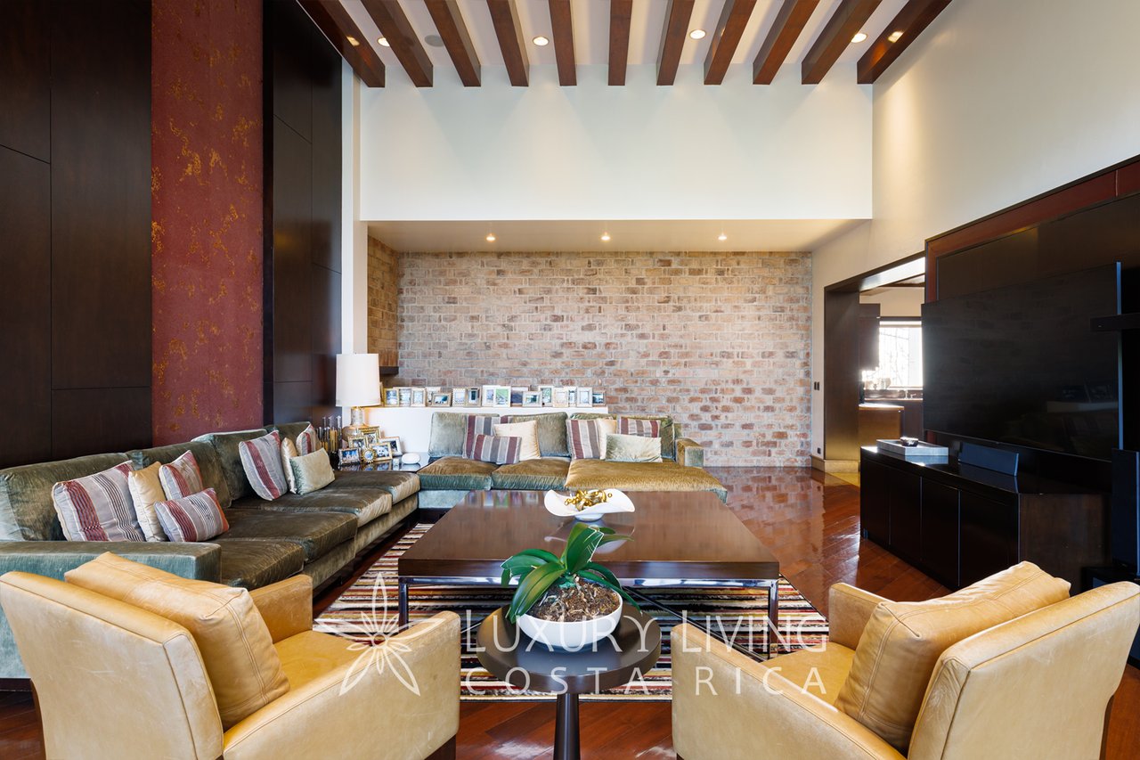 Living room with exposed ceiling beams, a brick accent wall and a large sectional sofa.