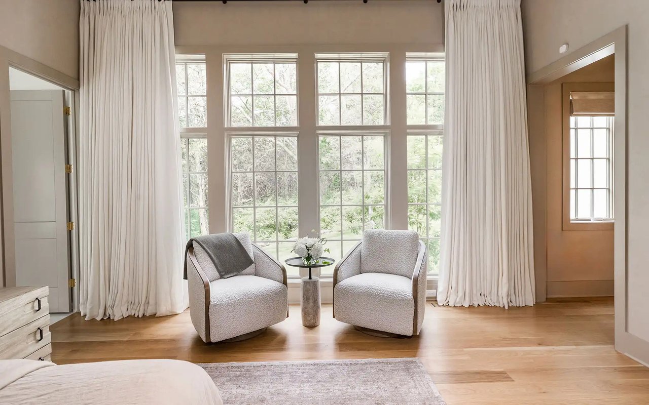 Bedroom seating area with two armchairs, tall windows, and floor-length white curtains.