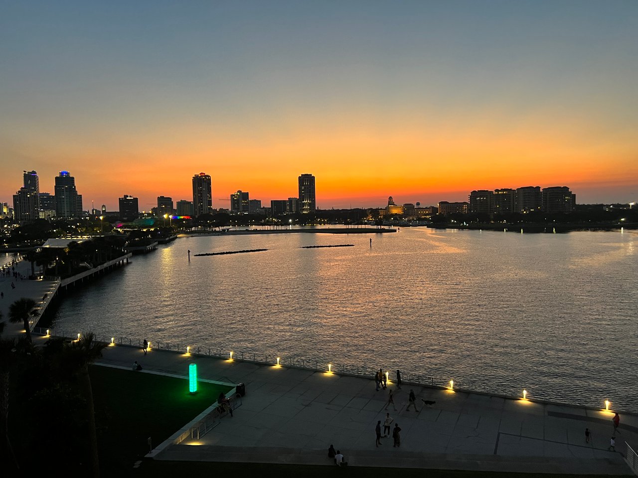 Waterfront skyline at dusk, with an orange sunset and illuminated promenade.