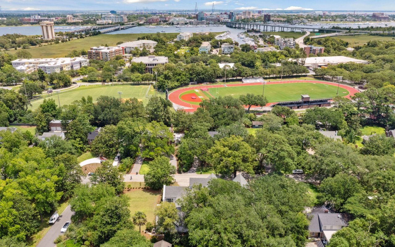 Aerial view of a leafy neighborhood with a sports field, waterway, and bridge.