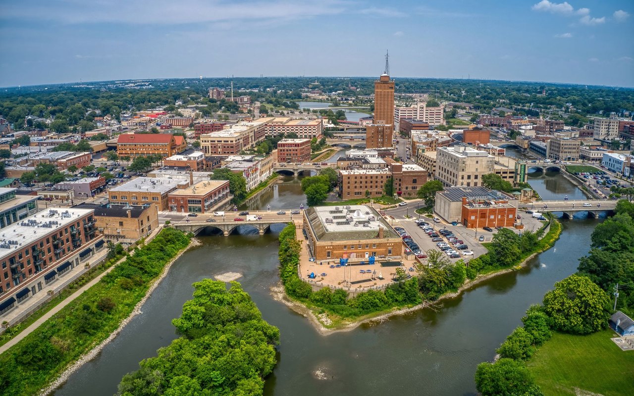Aerial view of downtown Aurora along the Fox River, with bridges and a tall brick tower.