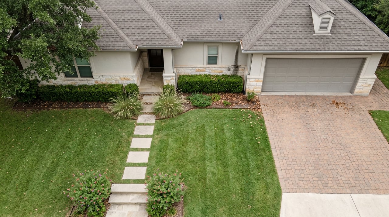 Overhead view of a suburban home with a paver driveway, striped lawn, mature oak, and limestone entry stoop.