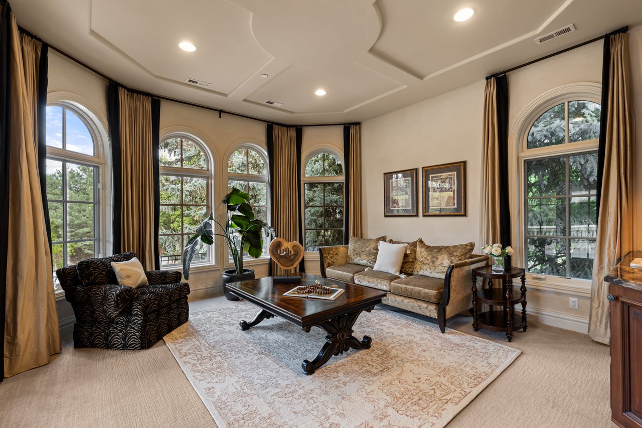 Furnished living room with arched windows, patterned seating, and a carved dark coffee table.