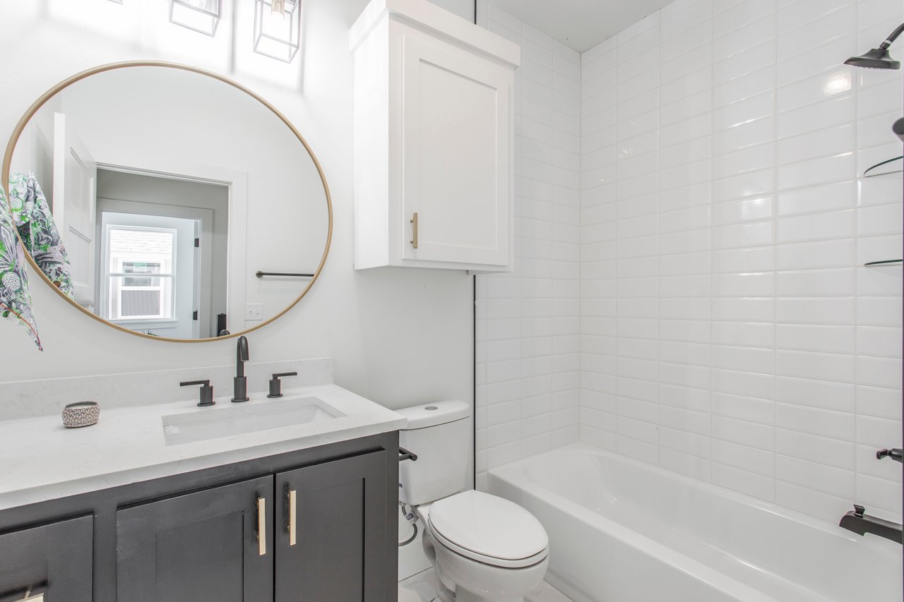 Bathroom with a white subway-tile tub and shower, dark vanity, and large brass-framed oval mirror.