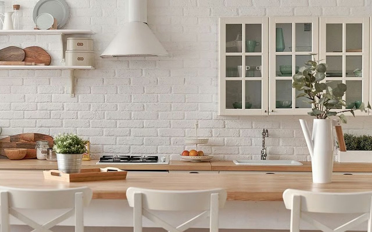 Bright white-brick kitchen with glass-front cabinets, a gas cooktop, and a broad wooden island.