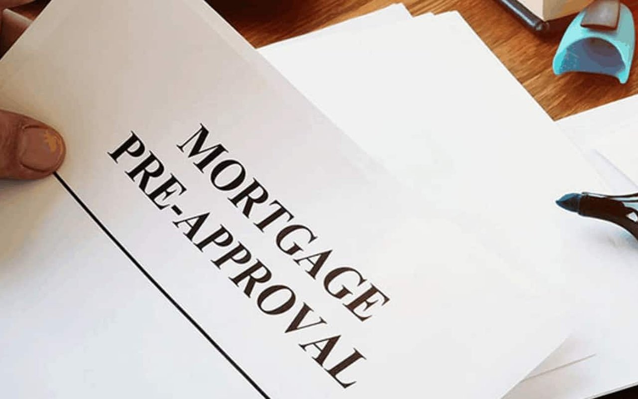 Mortgage pre-approval paperwork held over a wooden desk beside a pen.