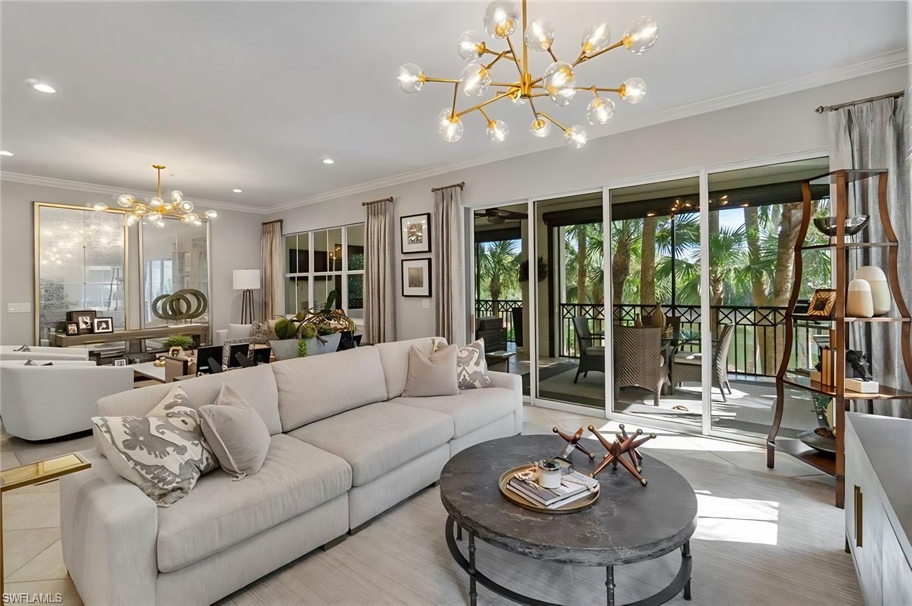 Living room with a pale sectional, sculptural chandeliers, and sliding doors to a palm-lined patio.