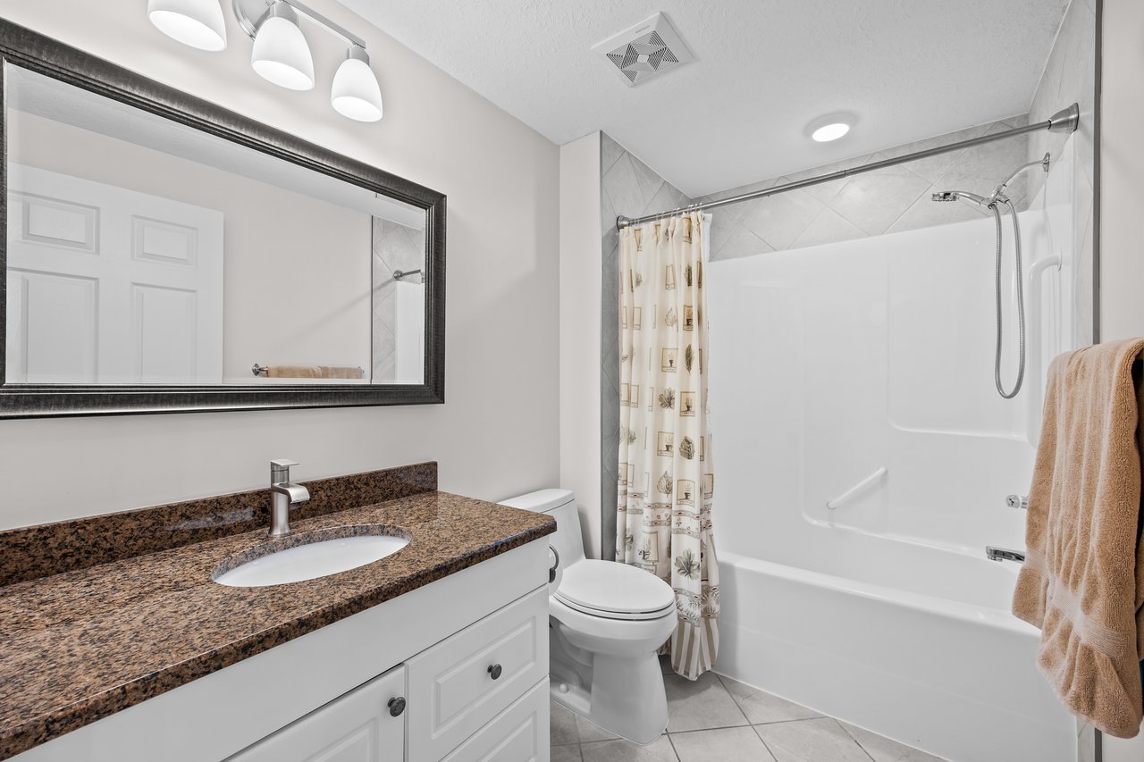 Bathroom with a granite vanity, large mirror, and white tub-shower.
