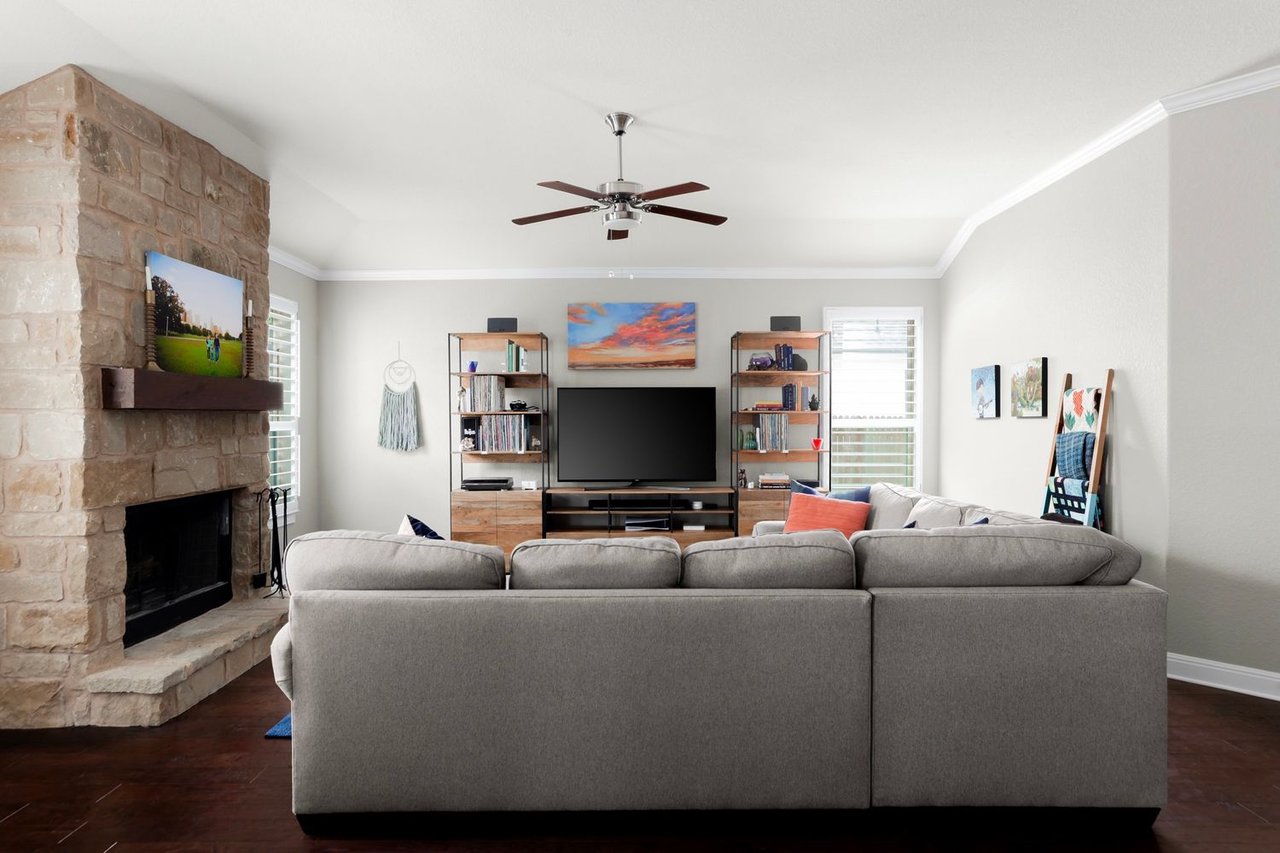 Living room with a gray sectional sofa, stone fireplace, and dark wood flooring.